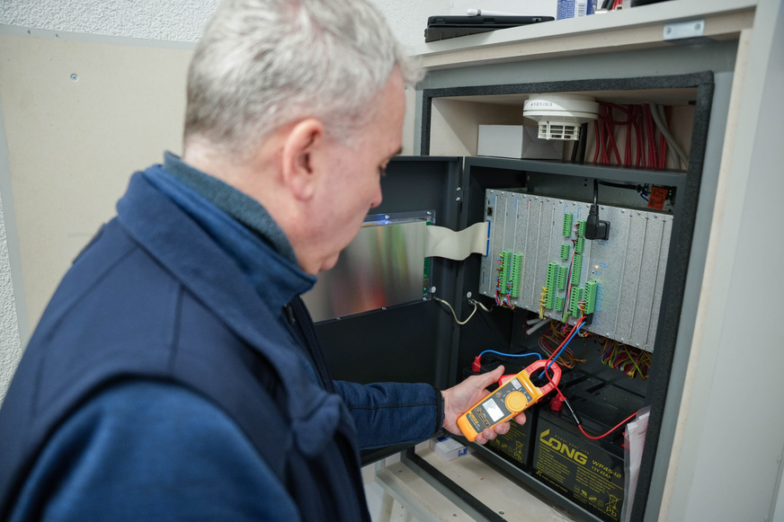 Bild 2 Ein TÜV-SÜD-Sachverständiger prüft die Brandmelderzentrale auf Alarm- und Ruhestrom, Um sicherzustellen, dass die Batterien bei Stromausfall die Funktionsfähigkeit der Anlage gewährleisten. Bei der Energieversorgung bestehen oft Mängel.