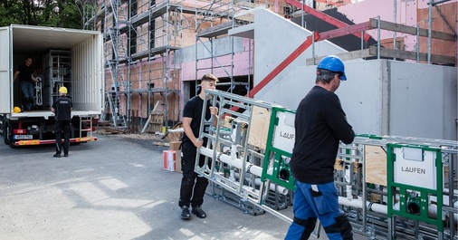 „Ingenieure und Techniker installieren vernetzte Gebäudetechnik auf einer Baustelle. Im Hintergrund sind digitale Steuerungssysteme und Energiemodule zu erkennen, die für intelligente Energieverteilung und Smart Building Technologien genutzt werden. - © LAUFEN