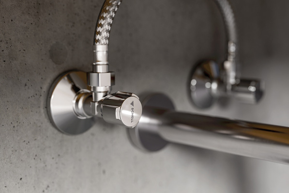 Nahaufnahme von zwei verchromten Wasserabsperrventilen, die an geflochtenen Schläuchen an einer grauen Betonwand befestigt sind. - © Schell