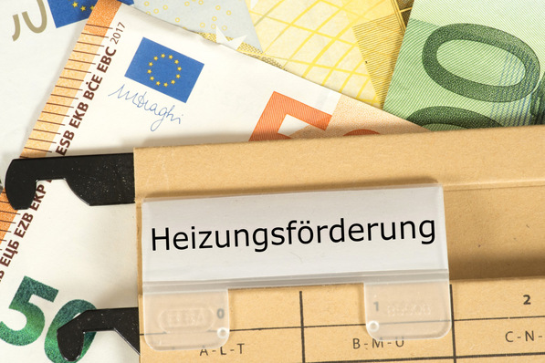 Alt-Text: „Symbolbild für Fördergelder in der Gebäudetechnik: Ein Briefumschlag mit der Aufschrift 'Heizungsförderung' liegt neben Euro-Scheinen und einem Klemmbrett – thematisierte finanzielle Unterstützung für nachhaltige und energieeffiziente Heizsysteme.“. - © studio v-zwoelf – stock.adobe.com