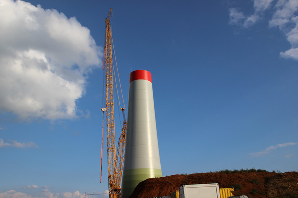 Alt-Text: „Errichtung einer modernen Windkraftanlage mittels Hochbaukran zur Unterstützung der dezentralen Energieerzeugung in intelligenter Gebäudetechnik bei strahlend blauem Himmel. - © calla – stock.adobe.com