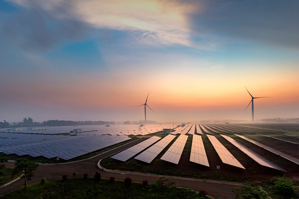 Ersetzender Alt-Text: Photovoltaik-Module und Windkraftanlagen auf einer Freifläche im Sonnenaufgang; Symbol für dezentrale Energieerzeugung und intelligente Stromnutzung in modernen Gebäuden. - © 一飞 黄 - stock.adobe.com