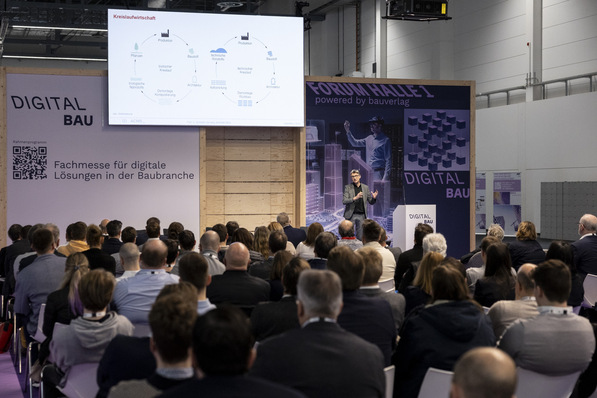 Ein Redner präsentiert einem sitzenden Publikum auf einer Messe für digitales Bauen ein Diagramm der Kreislaufwirtschaft. - © Messe München