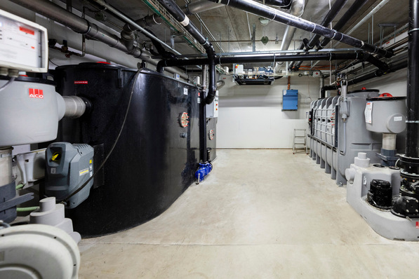 Raum mit großen schwarzen Tanks, Rohren und Industrieanlagen an den Wänden, wahrscheinlich ein Gebäudeversorgungsbereich. - © ACO Haustechnik